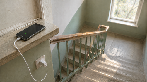 Ein älteres Android-Handy auf einem Fensterbrett im Treppenhaus, per Kabel mit Strom versorgt